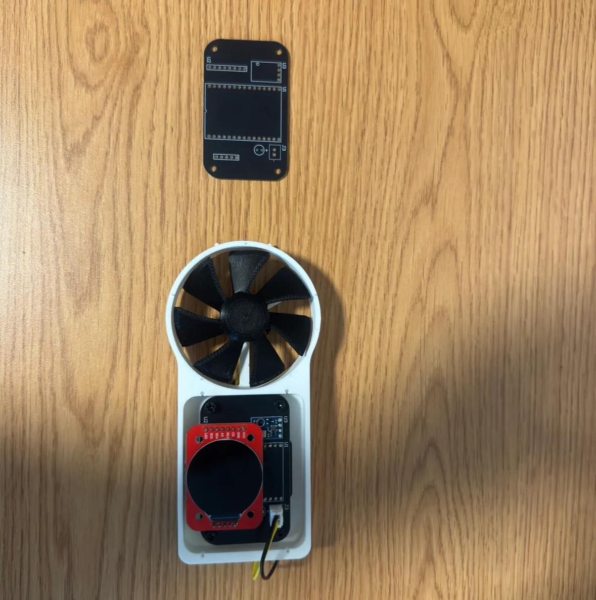 The anemometer on a workbench — the bare control board above, and the assembled unit below with a printed ducted impeller and a round display on the back.
