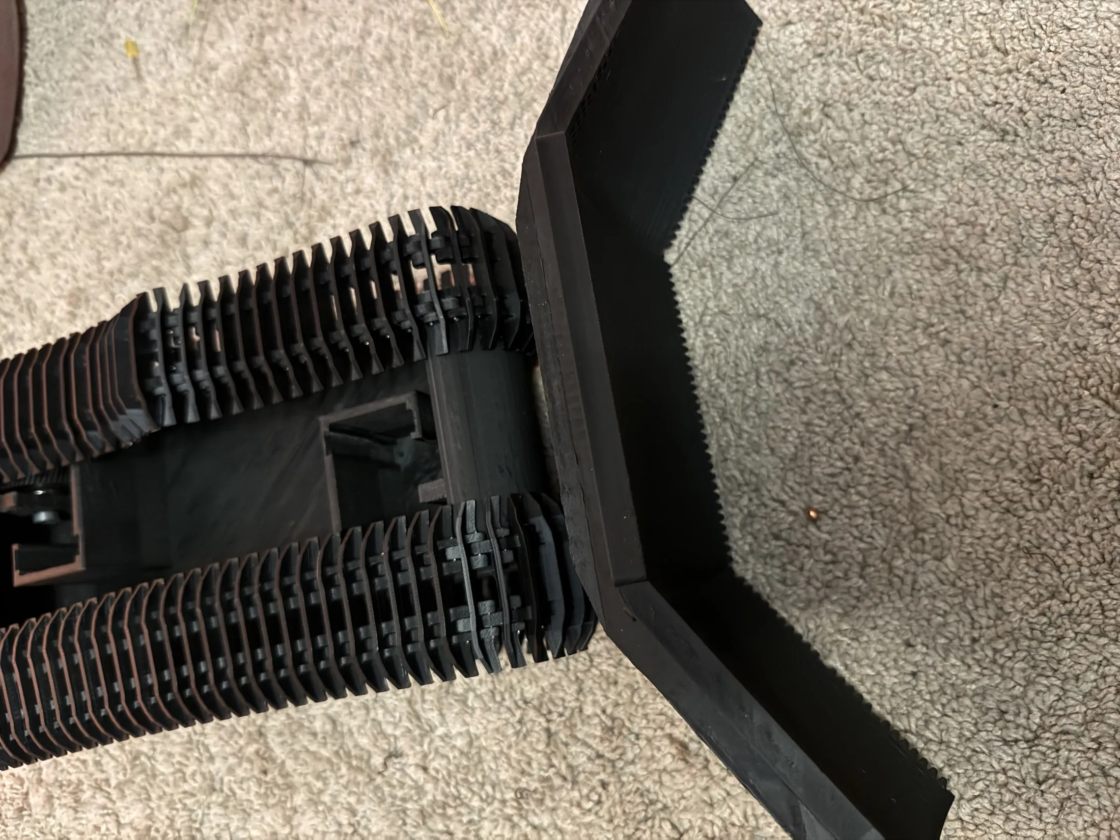 Top-down view of the snowcat's two printed tracks and the black front blade on carpet.